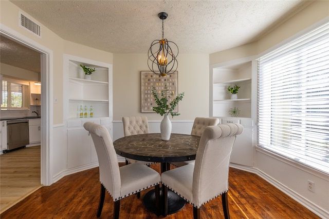 dining space with a textured ceiling, built in shelves, dark wood-type flooring, and a chandelier