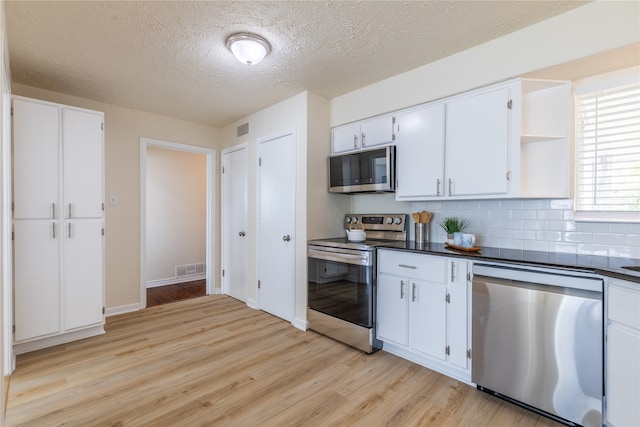 kitchen with appliances with stainless steel finishes, light wood-type flooring, white cabinetry, and backsplash