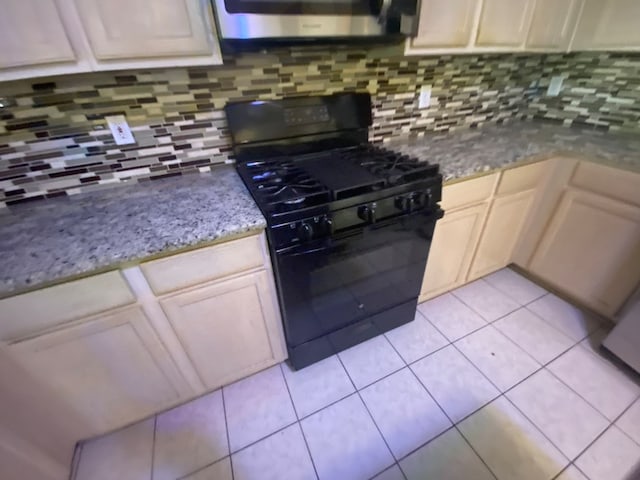 kitchen with black gas range, backsplash, light stone countertops, and light tile patterned floors