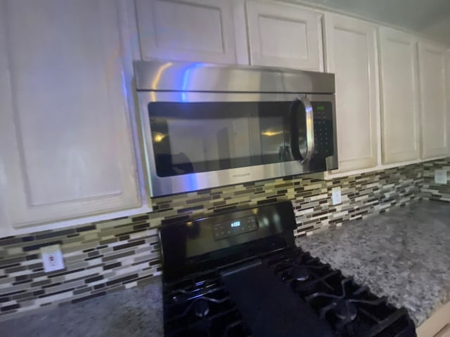 room details featuring gas stove, decorative backsplash, white cabinetry, and light stone countertops