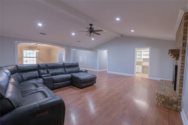 living room featuring ornamental molding, ceiling fan with notable chandelier, hardwood / wood-style flooring, a fireplace, and vaulted ceiling with beams