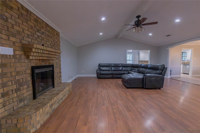 living room with ceiling fan, a brick fireplace, vaulted ceiling with beams, hardwood / wood-style flooring, and ornamental molding