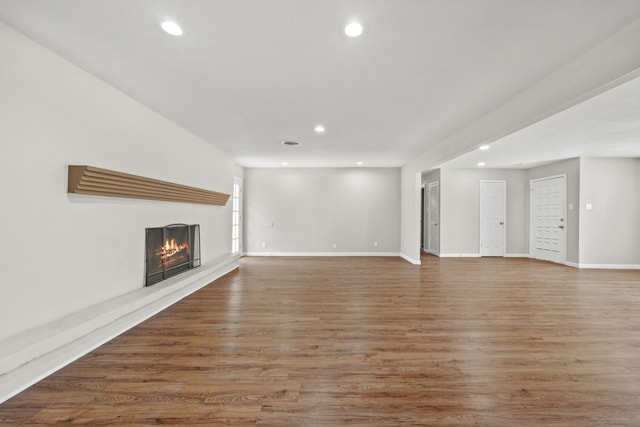 unfurnished living room with a lit fireplace, wood finished floors, and recessed lighting