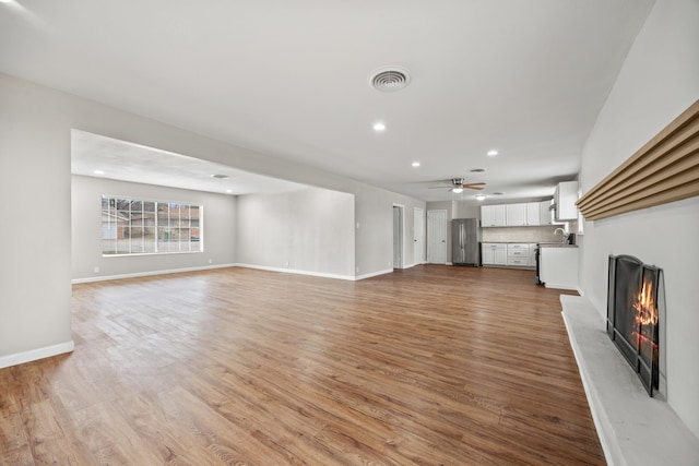 unfurnished living room featuring a lit fireplace, visible vents, light wood-style flooring, and baseboards