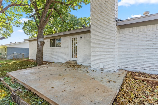 entrance to property featuring brick siding, a patio, a chimney, and fence