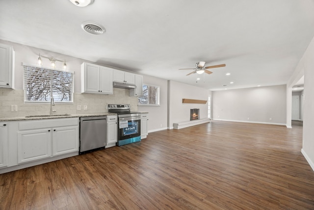 kitchen with stainless steel appliances, open floor plan, white cabinetry, a sink, and under cabinet range hood