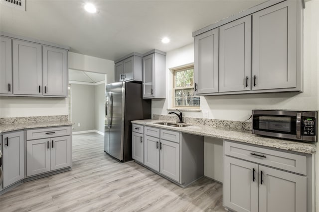 kitchen with sink, gray cabinets, appliances with stainless steel finishes, light hardwood / wood-style floors, and light stone counters