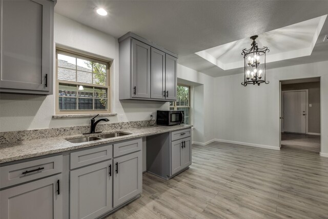 kitchen featuring appliances with stainless steel finishes, light hardwood / wood-style floors, a tray ceiling, sink, and gray cabinets