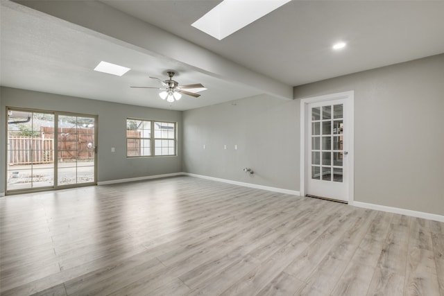 unfurnished room with beamed ceiling, ceiling fan, a skylight, and light hardwood / wood-style flooring