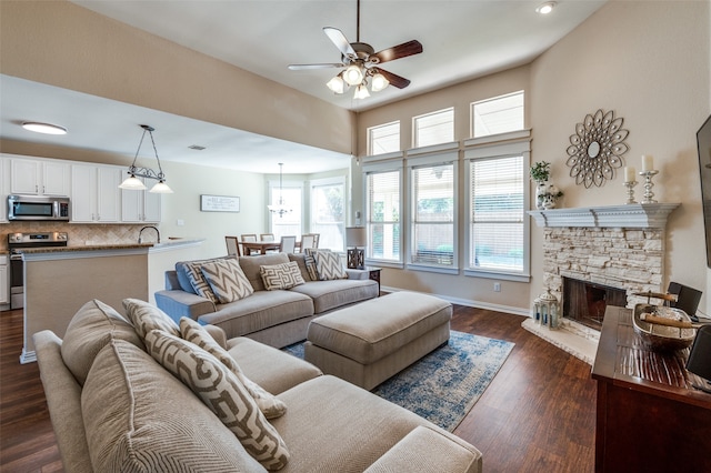 living room featuring dark hardwood / wood-style flooring, ceiling fan, and a stone fireplace