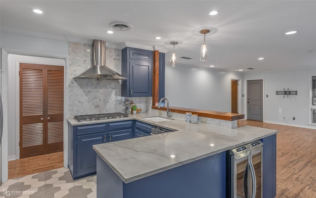 kitchen with kitchen peninsula, sink, pendant lighting, and wall chimney range hood