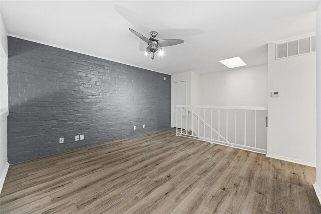 unfurnished room featuring hardwood / wood-style floors, ceiling fan, and brick wall