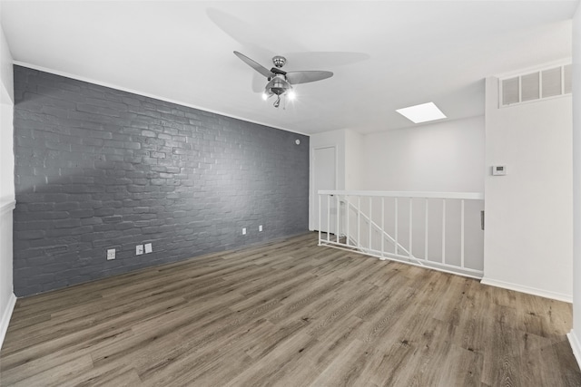 spare room featuring brick wall, a skylight, hardwood / wood-style flooring, and ceiling fan