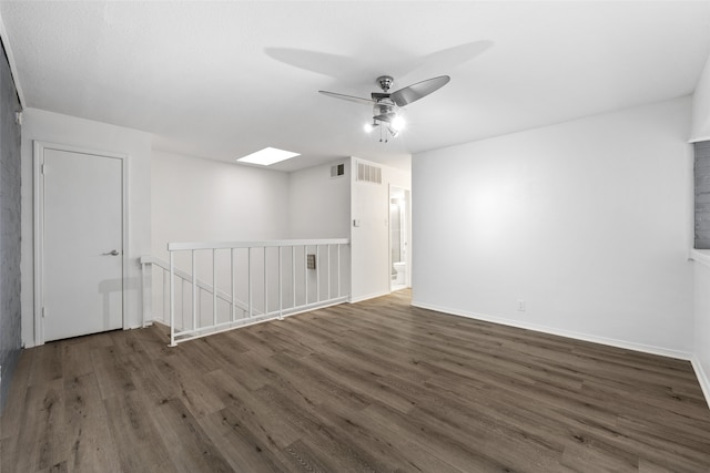 empty room featuring dark hardwood / wood-style flooring, a skylight, and ceiling fan