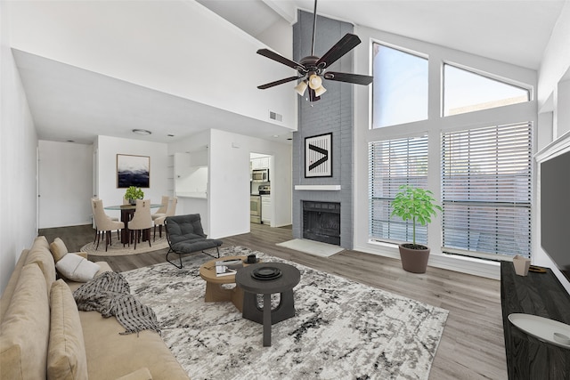 living room featuring a fireplace, ceiling fan, light hardwood / wood-style flooring, and high vaulted ceiling