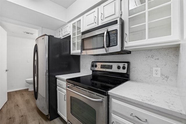 kitchen with white cabinets, appliances with stainless steel finishes, tasteful backsplash, light hardwood / wood-style floors, and light stone counters