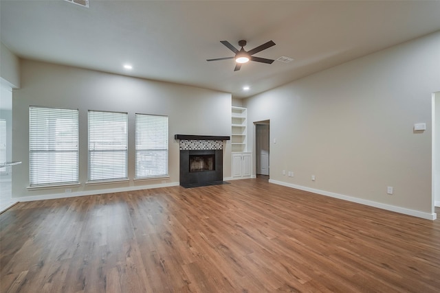 unfurnished living room with ceiling fan, wood-type flooring, built in shelves, and a tiled fireplace