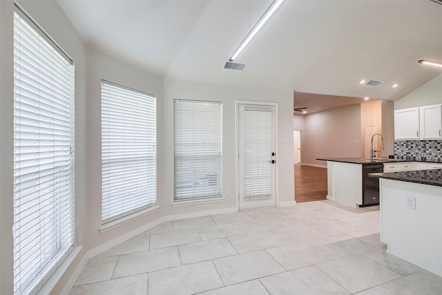 kitchen with black dishwasher, white cabinets, kitchen peninsula, vaulted ceiling, and light tile patterned floors