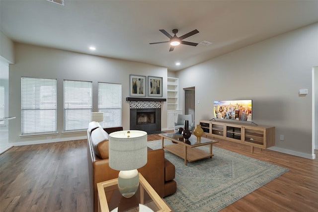 living room featuring a tile fireplace, wood-type flooring, ceiling fan, and built in shelves