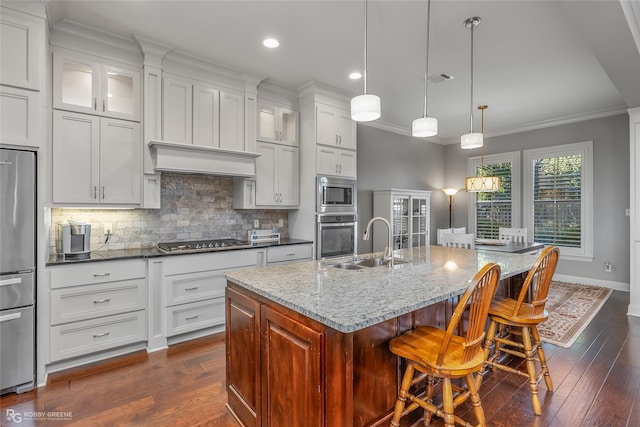 kitchen with appliances with stainless steel finishes, light stone counters, dark wood-type flooring, a center island with sink, and white cabinets