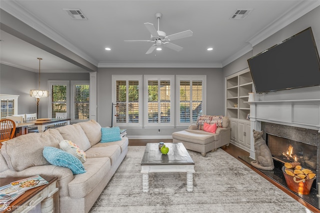 living room with a lit fireplace, visible vents, wood finished floors, and ornamental molding