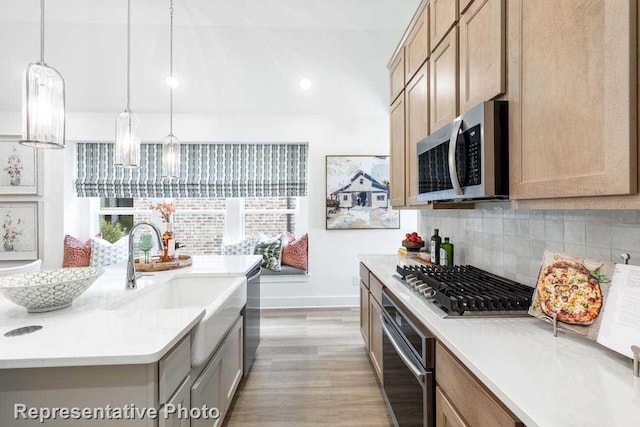 kitchen with decorative backsplash, light wood-type flooring, stainless steel appliances, sink, and pendant lighting