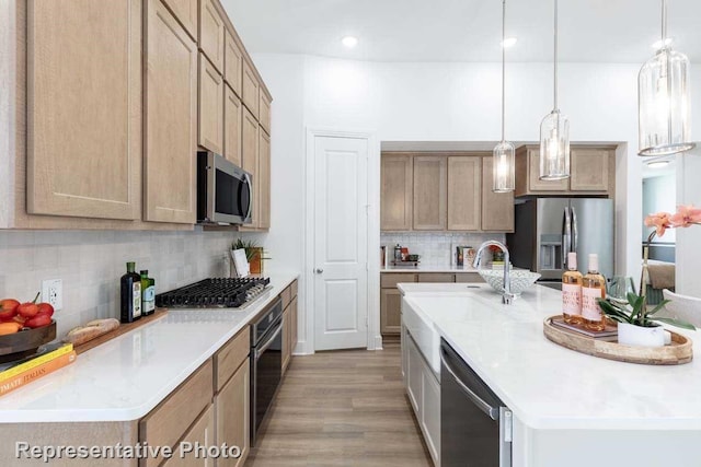 kitchen with hanging light fixtures, tasteful backsplash, a kitchen island with sink, appliances with stainless steel finishes, and light wood-type flooring