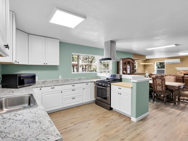 kitchen with island range hood, stainless steel appliances, a sink, an AC wall unit, and light countertops