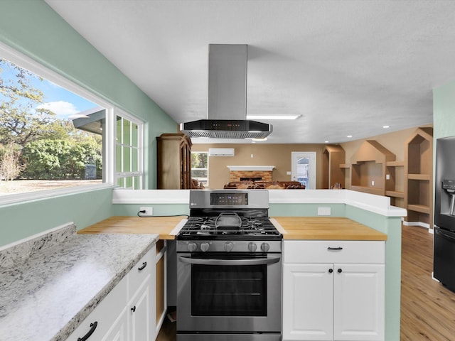 kitchen featuring white cabinets, stainless steel range with gas cooktop, island exhaust hood, and wood counters