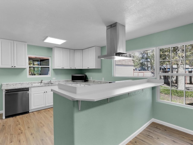 kitchen with light countertops, appliances with stainless steel finishes, white cabinets, a sink, and island range hood