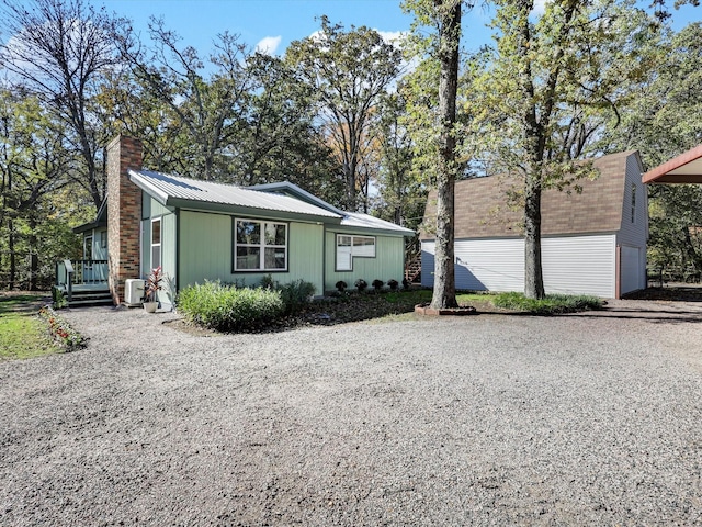 view of front facade with a chimney, an outdoor structure, gravel driveway, metal roof, and a garage
