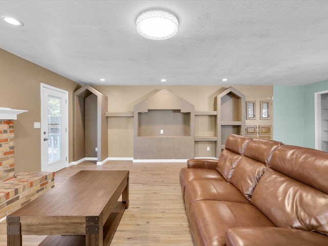 living area with recessed lighting, a brick fireplace, light wood-style flooring, and a textured ceiling