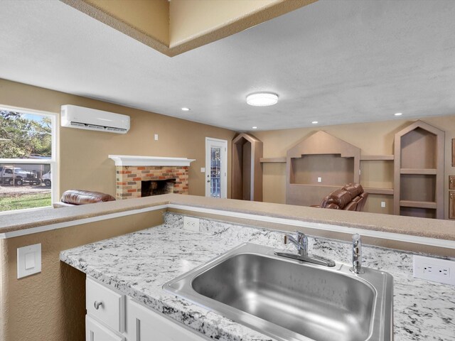 kitchen featuring a brick fireplace, open floor plan, a wall mounted air conditioner, and a sink