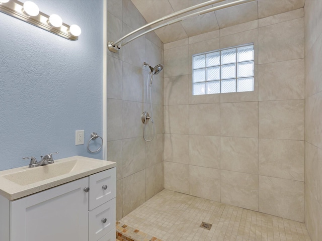 bathroom with a textured wall, a tile shower, and vanity