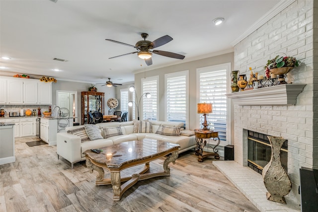 living room featuring ceiling fan, light hardwood / wood-style flooring, ornamental molding, and a brick fireplace