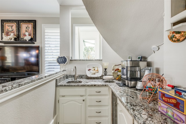 kitchen with light stone counters, sink, white cabinets, and ornamental molding