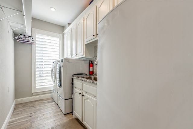 clothes washing area with cabinets, washing machine and dryer, and light hardwood / wood-style floors