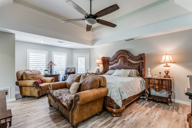 bedroom with light wood-type flooring, a raised ceiling, ceiling fan, and crown molding