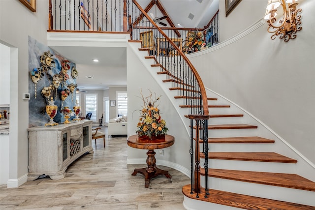 stairway with a towering ceiling, wood-type flooring, and ceiling fan with notable chandelier