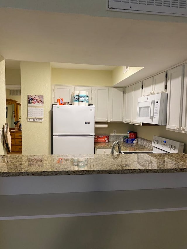 kitchen with white appliances, white cabinetry, and dark stone counters