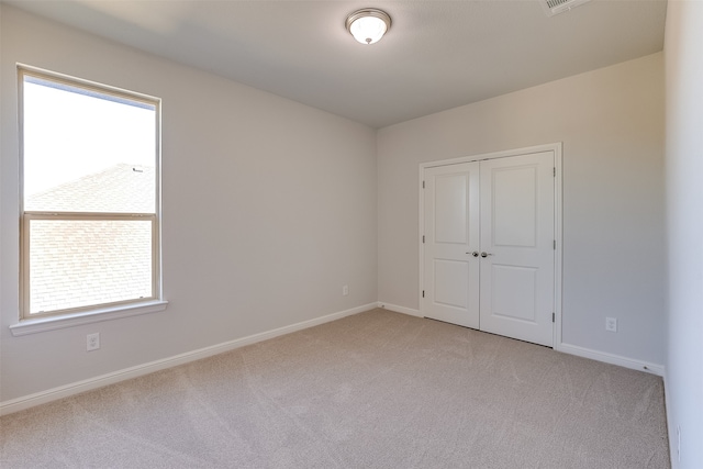 unfurnished bedroom with multiple windows, light carpet, and a closet