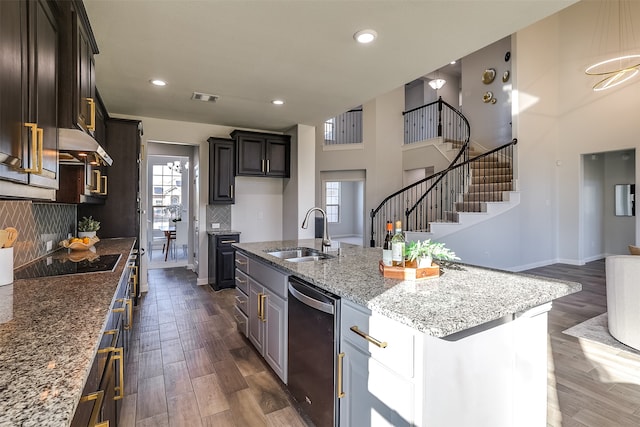 kitchen featuring dark wood-type flooring, dishwasher, a center island with sink, and dark stone counters