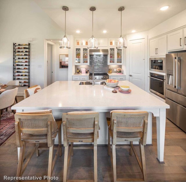 kitchen with a kitchen island with sink, pendant lighting, white cabinets, and stainless steel appliances