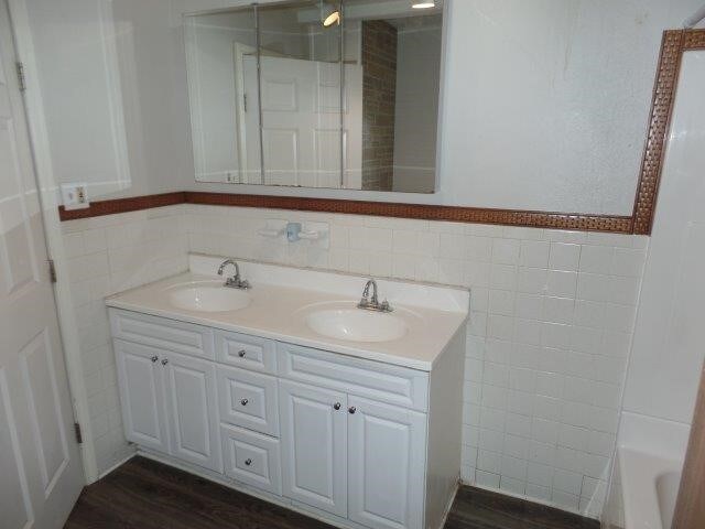 bathroom with a bath, vanity, wood-type flooring, and tile walls