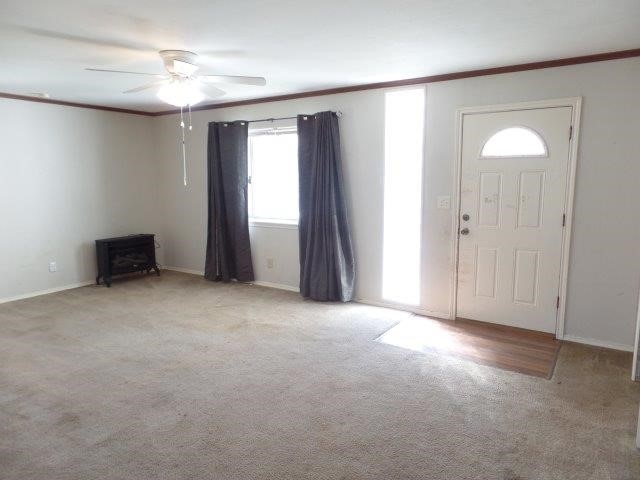 carpeted foyer featuring a wood stove, a wealth of natural light, crown molding, and ceiling fan