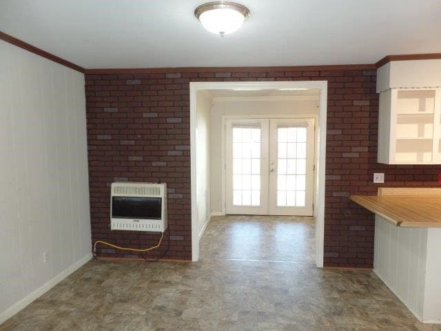 unfurnished living room featuring french doors, heating unit, crown molding, and brick wall