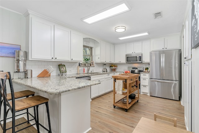 kitchen featuring light stone countertops, light wood-type flooring, white cabinetry, kitchen peninsula, and stainless steel appliances