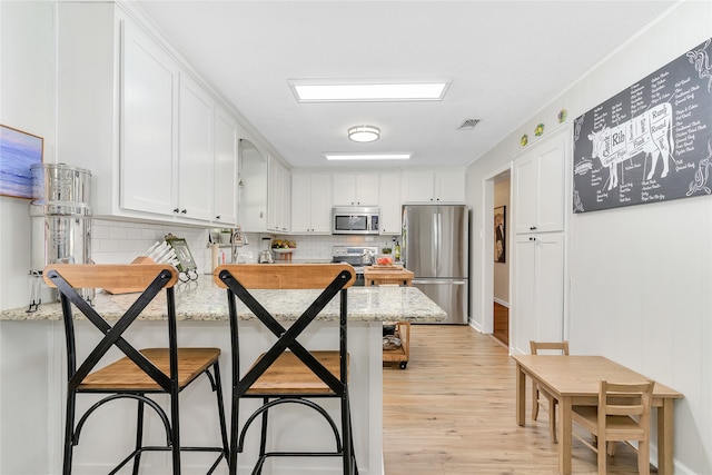 kitchen featuring a breakfast bar, backsplash, white cabinets, light stone counters, and stainless steel appliances