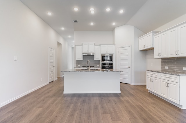 kitchen with appliances with stainless steel finishes, light hardwood / wood-style floors, white cabinetry, and light stone counters