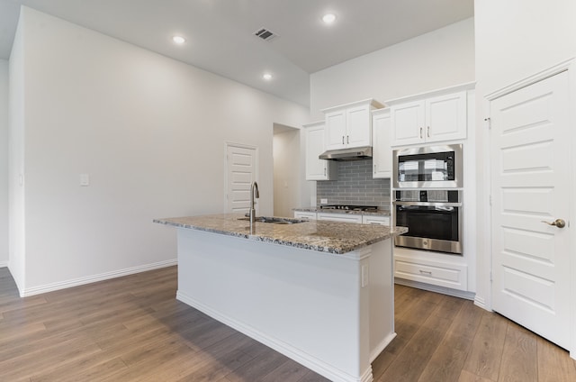 kitchen with white cabinetry, wood-type flooring, stone countertops, a kitchen island with sink, and appliances with stainless steel finishes